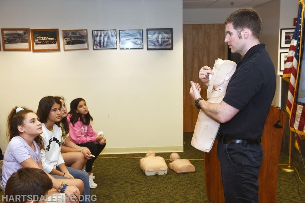 Instructor teaching CPR to a group using a manikin, with students attentively watching.
