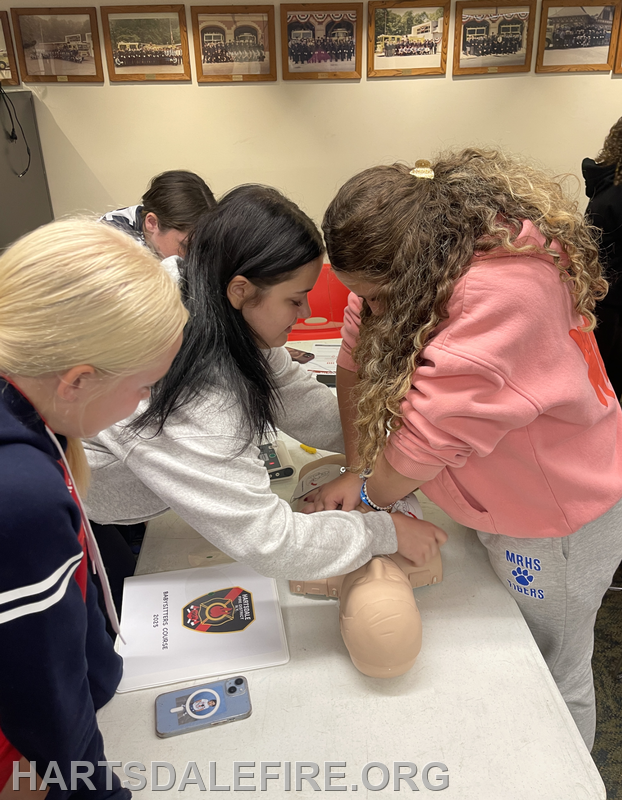 A group of young people practicing CPR techniques on a training mannequin in an educational setting.