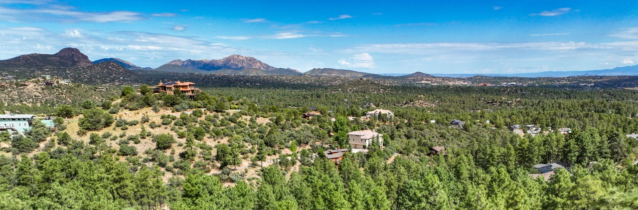 A scenic landscape with dense greenery, mountains in the background, and scattered homes under a bright blue sky.