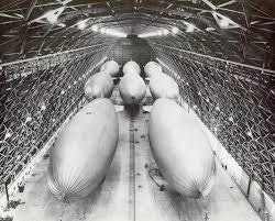 A large hangar with several airships lined up inside, showcasing a historical setting.