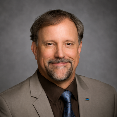 The image features a man with a friendly smile, dressed in a suit, with a grey background.