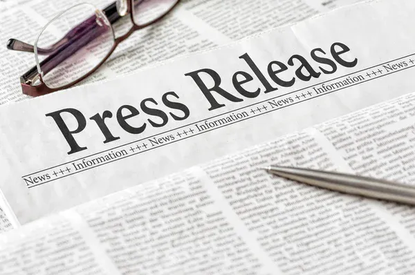 A newspaper with the headline "Press Release," a pair of glasses, and a pen.