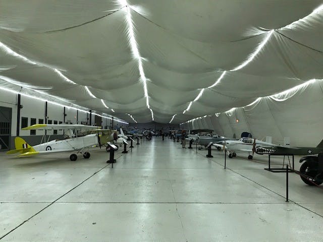 Aircraft displayed in a large hanger with a white ceiling, lined up on either side.