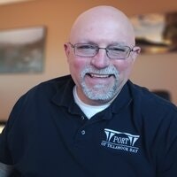 A smiling person wearing glasses and a "Port of Tacoma Bay" shirt.