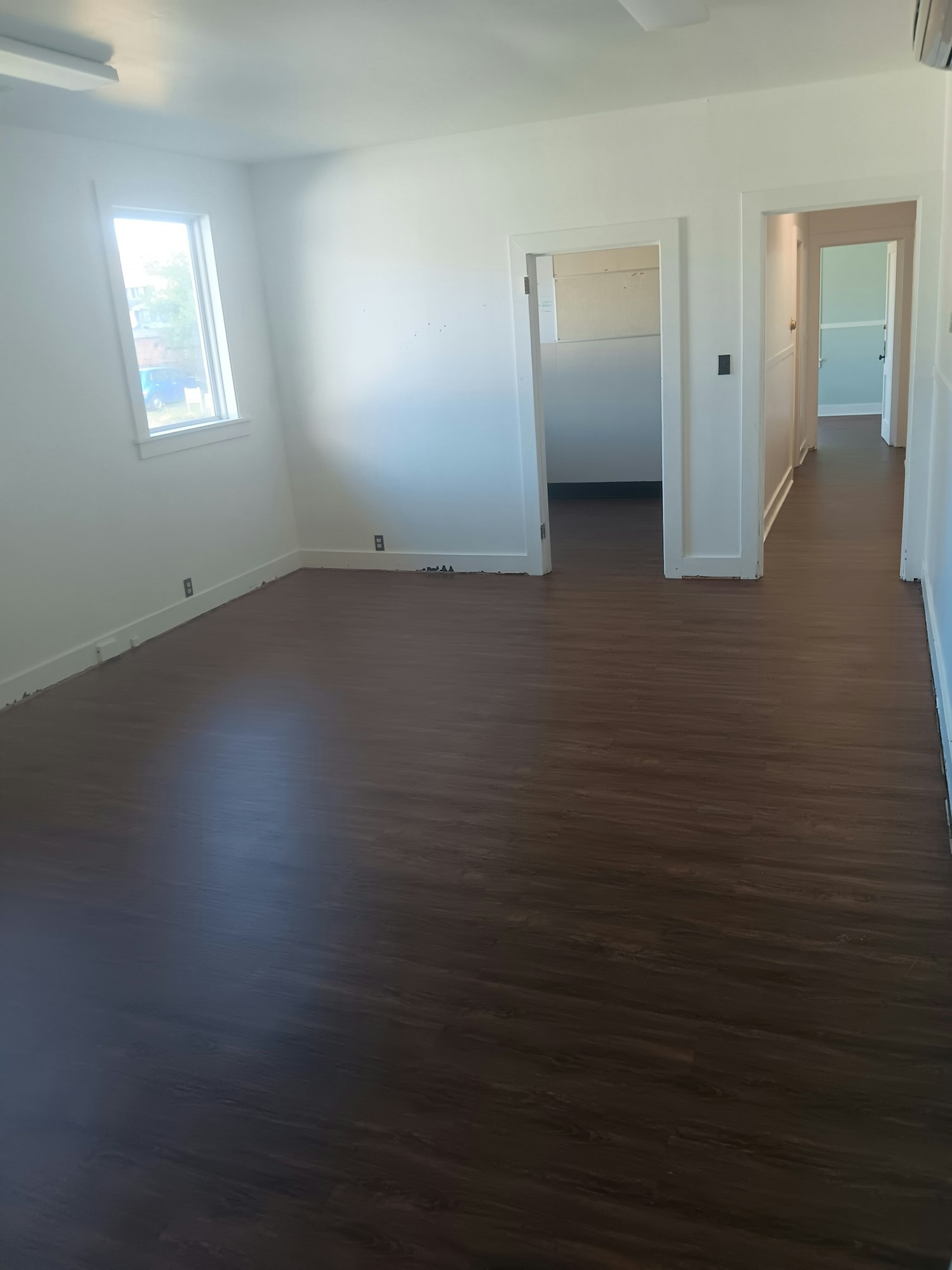 A room with dark wood flooring, white walls, and multiple doorways.