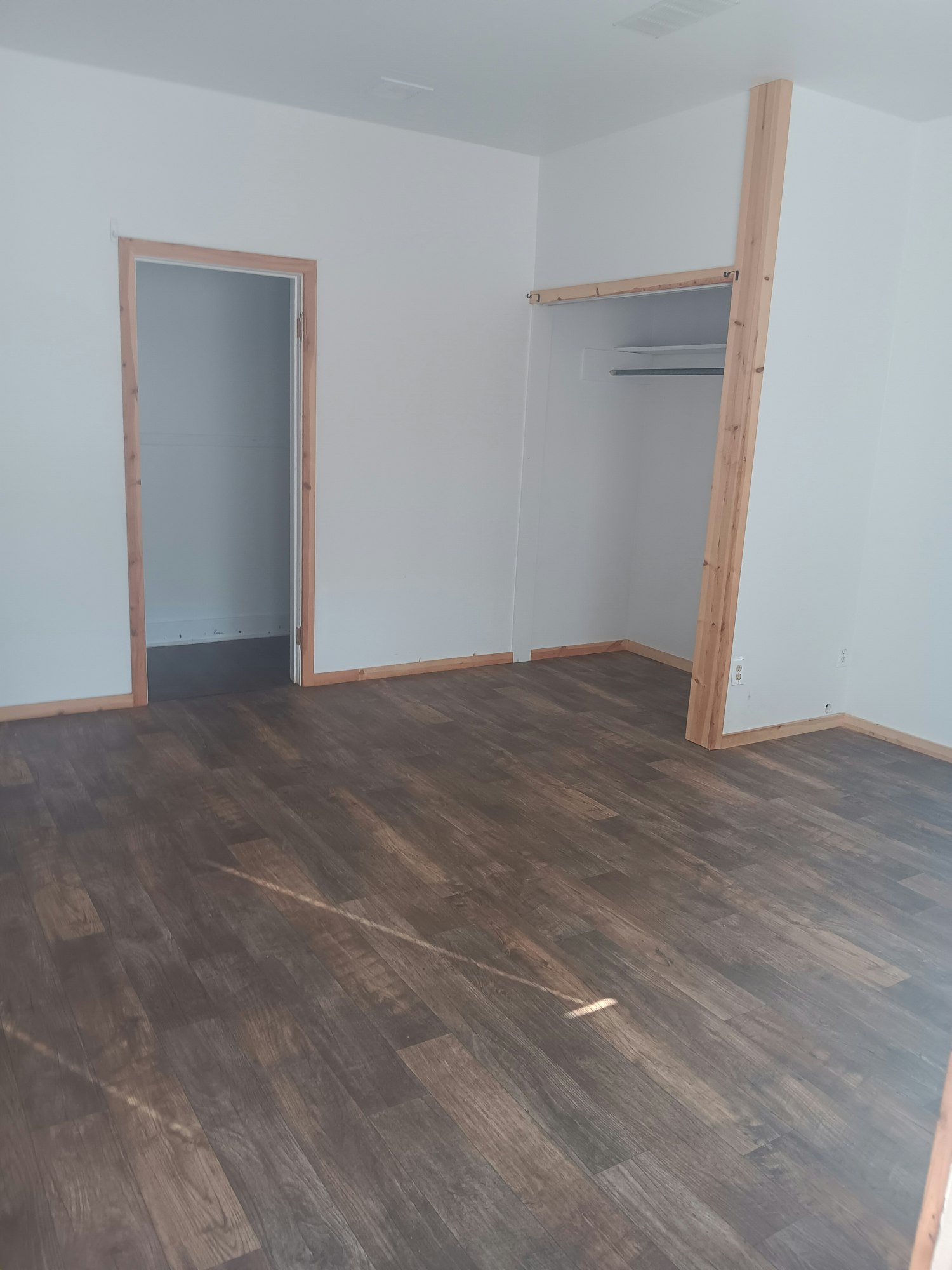 Empty room with wooden floor, white walls, and an open closet or storage area.
