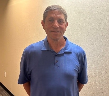A person wearing a blue polo shirt stands in a hallway with a light-colored wall.