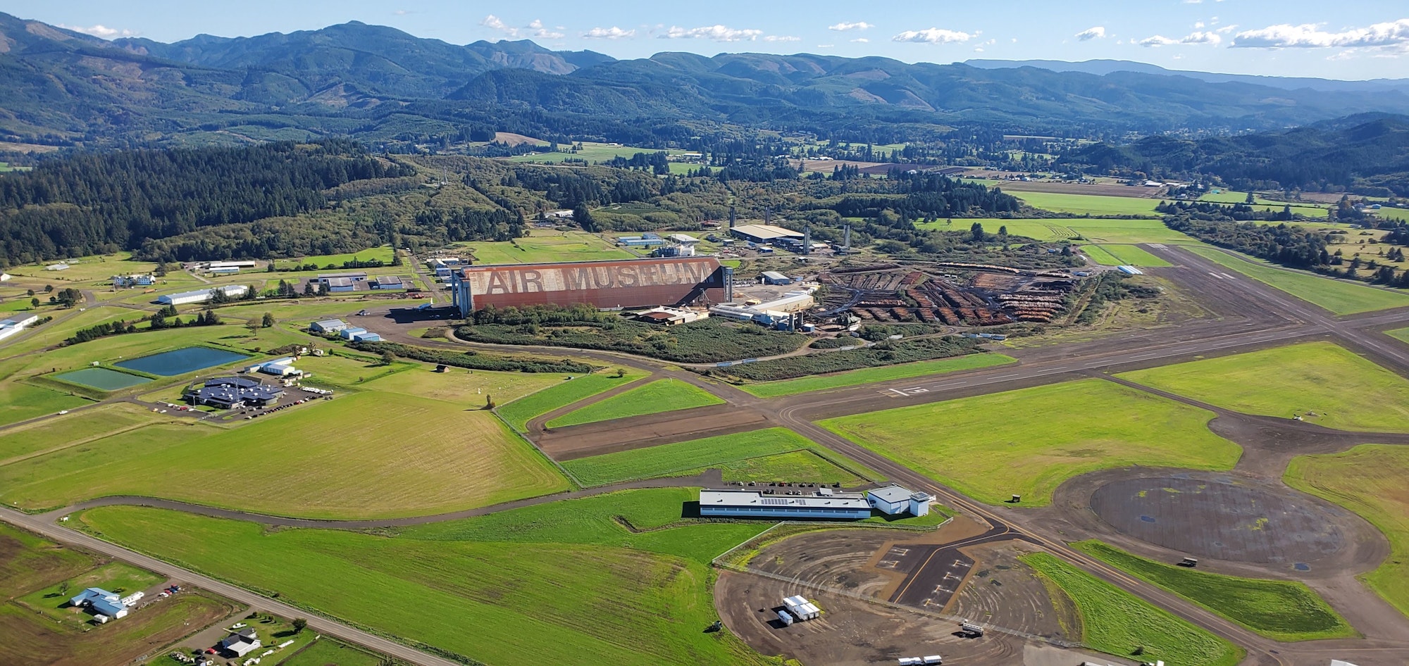 Aerial view of a large air museum building, runways, farmland, and hills in the distance.