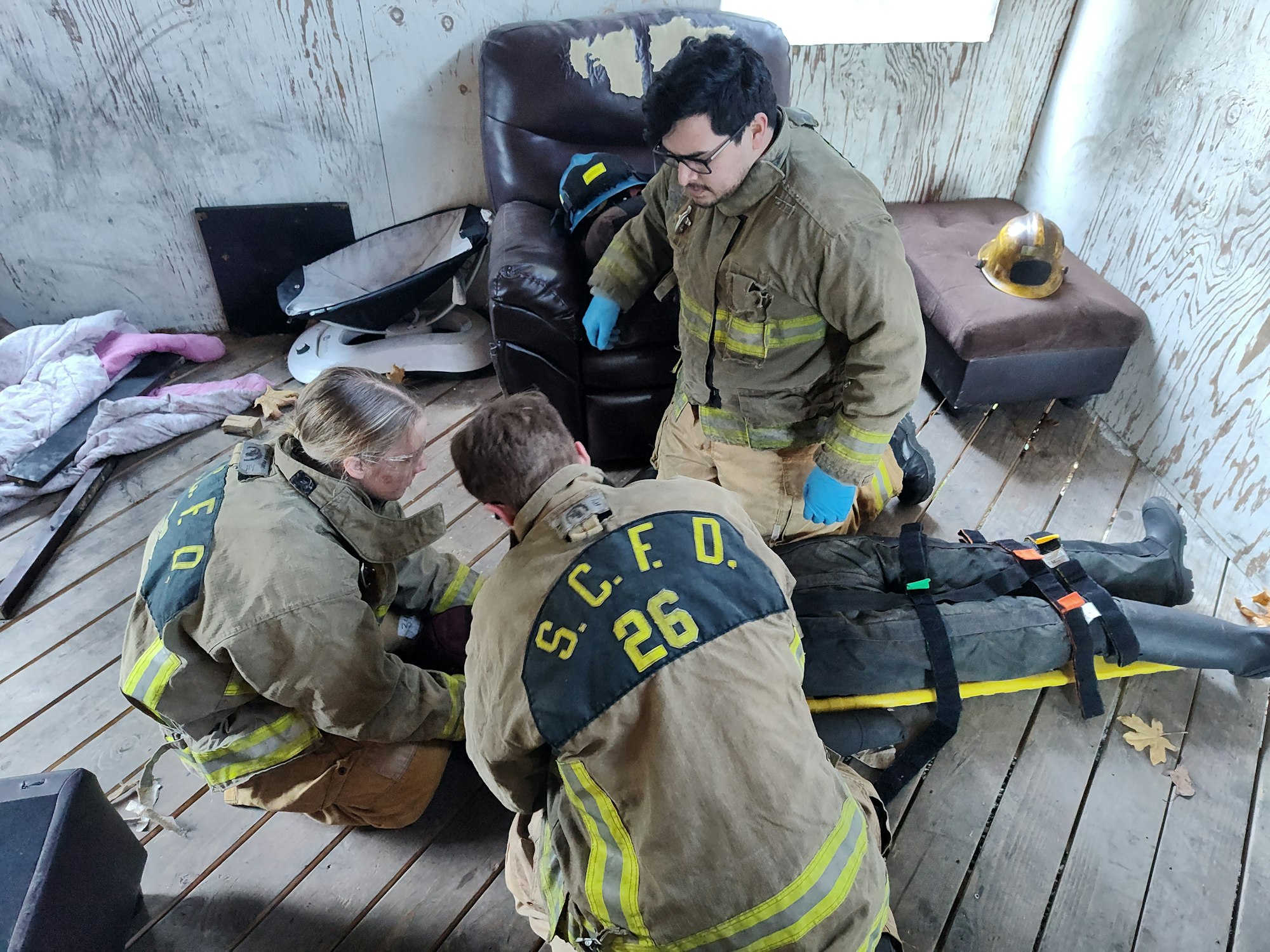 Firefighters training in a room, attending to a dummy on the floor.