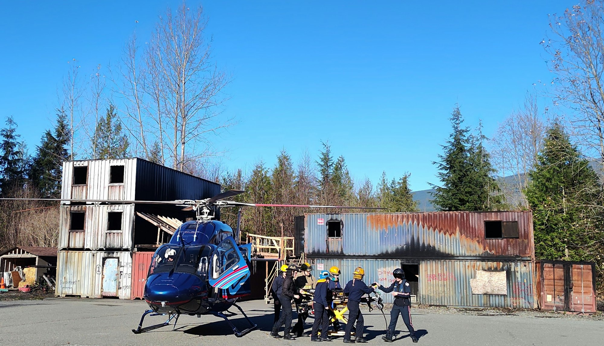A helicopter and emergency responders with a stretcher in a training or rescue simulation at an industrial site.