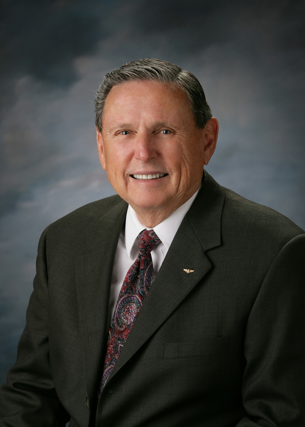 A man in a suit and tie, smiling against a neutral background.