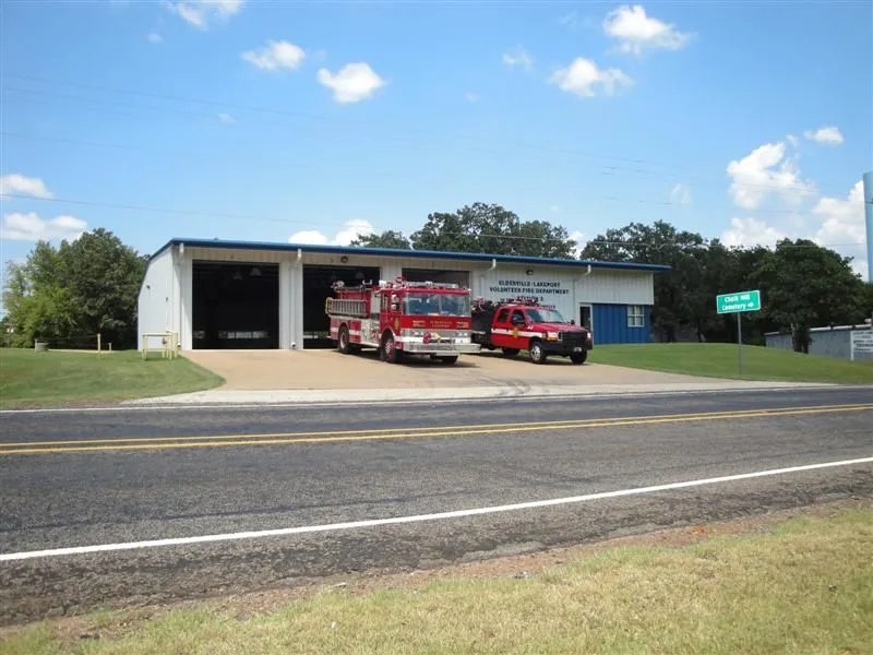 A fire station with a red fire truck and a service vehicle parked outside on a sunny day.