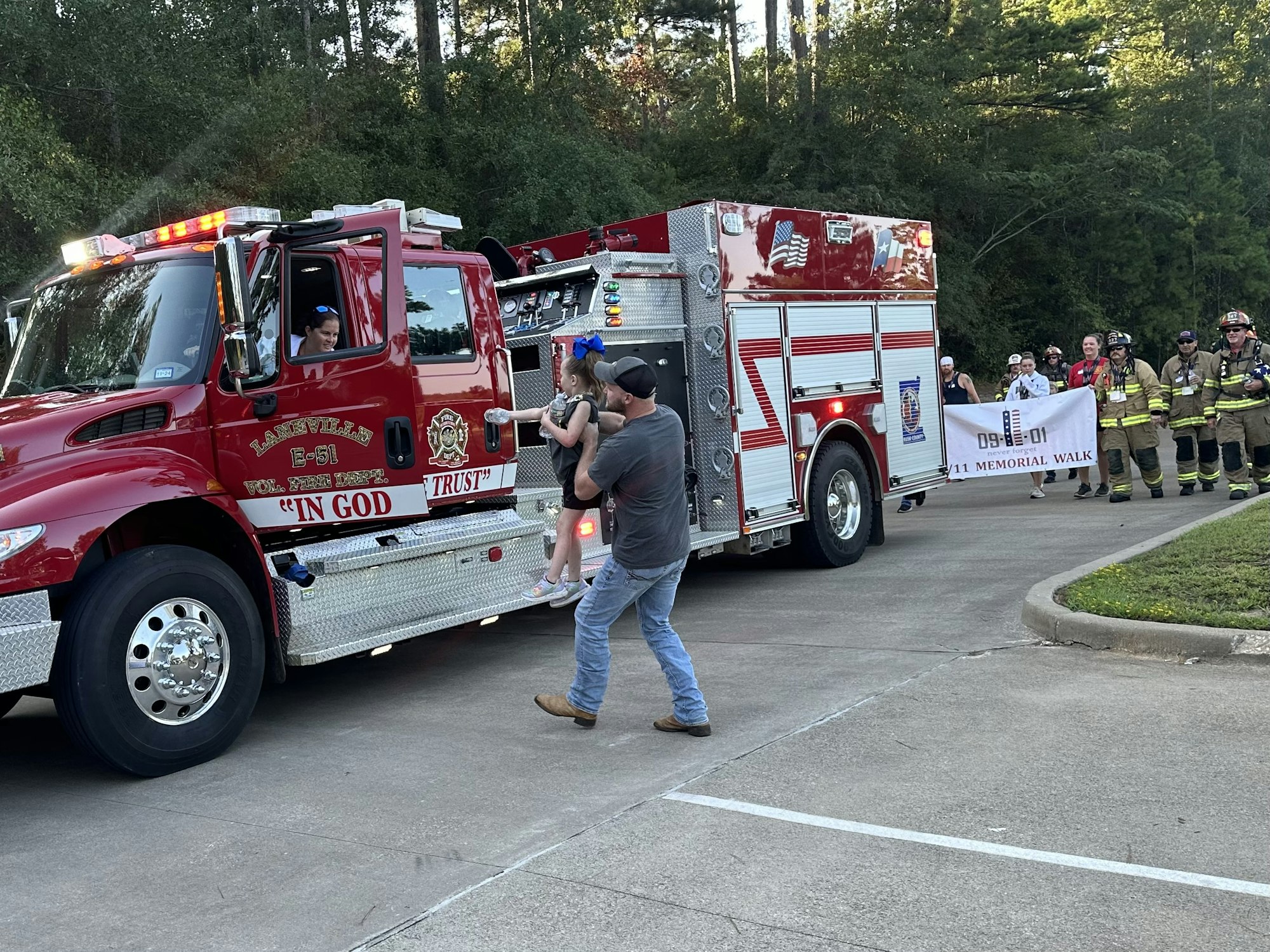 Firetruck with people nearby, a firefighter group holding a "9/11 Memorial Walk" banner.
