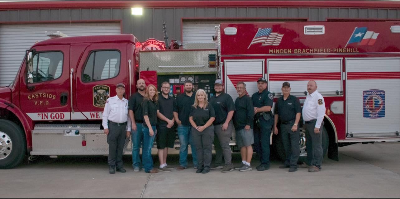 A group of firefighters stands in front of a fire truck, showcasing their teamwork and pride in their service.