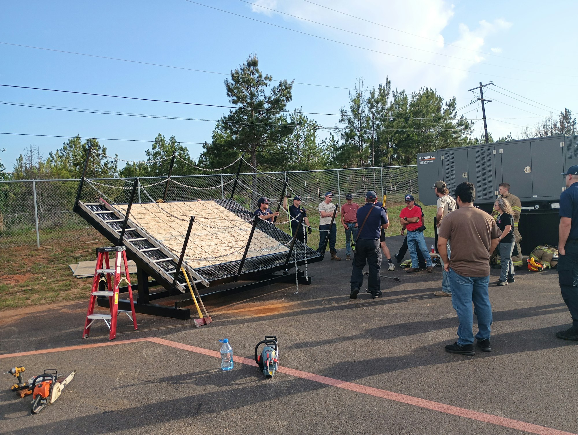 A group of people is gathered around a training setup with a sloped platform and safety equipment, likely for rescue drills.