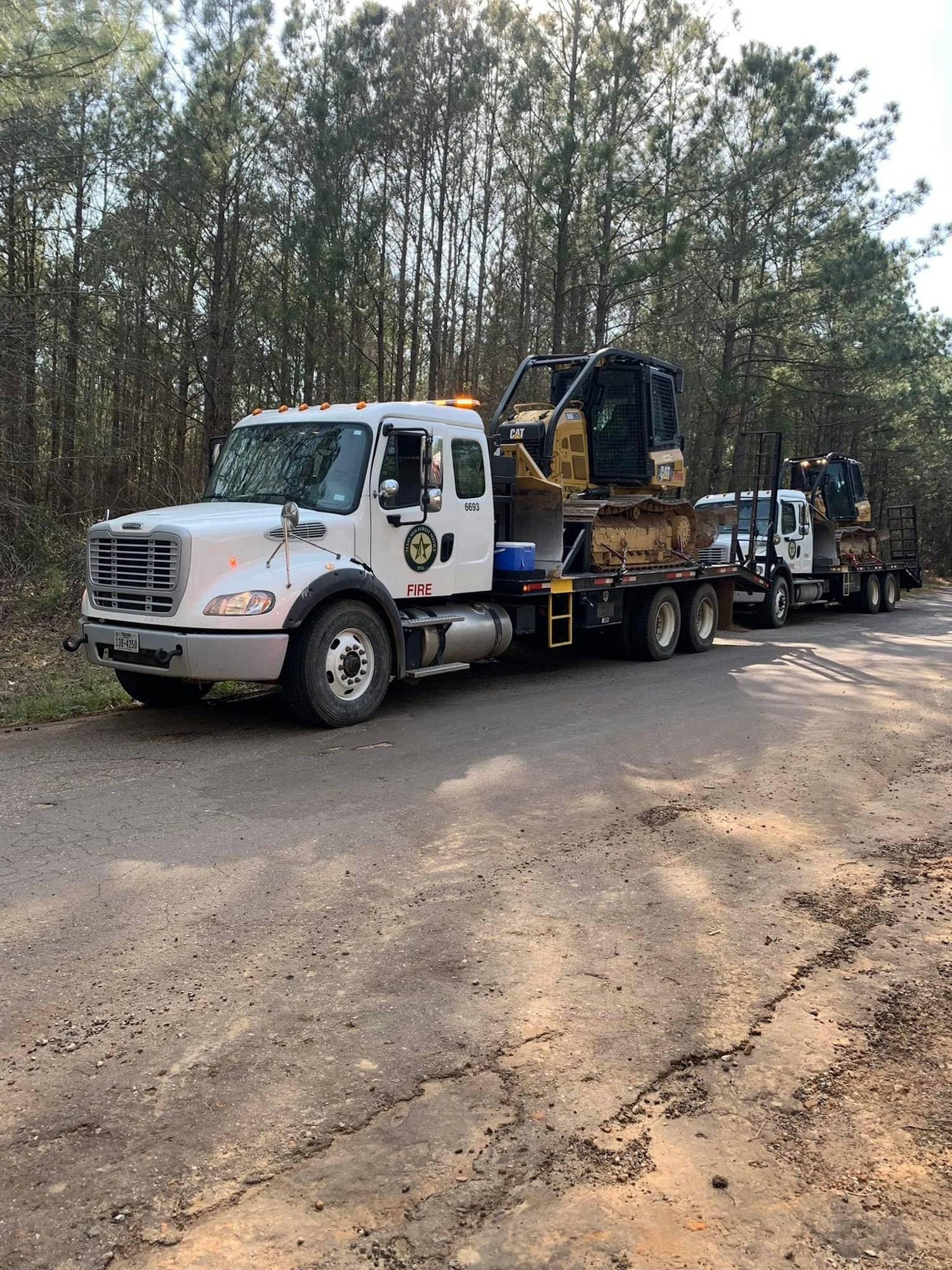 A fire department's flatbed truck hauling construction equipment on a forest road.