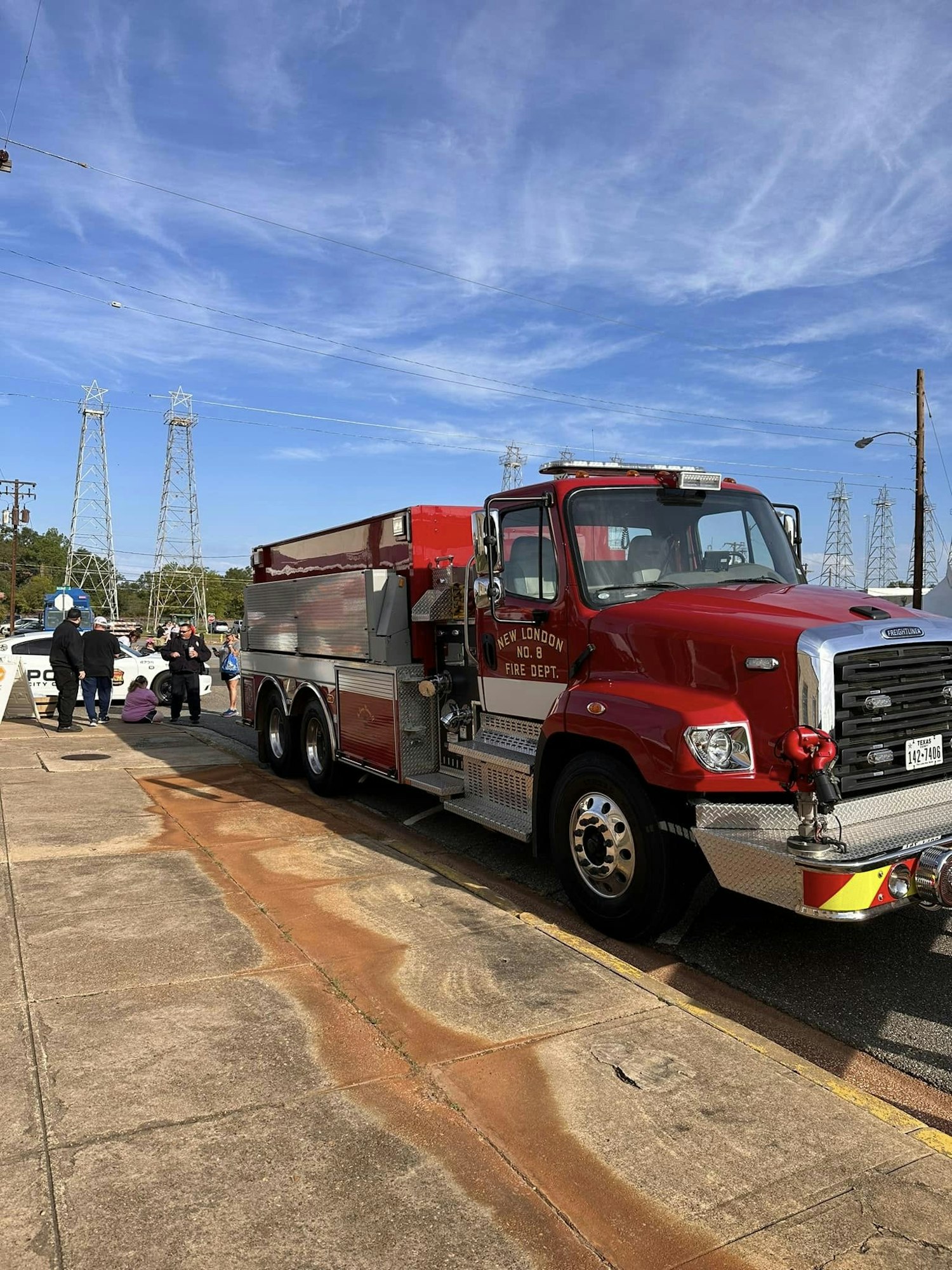 A red firetruck parked on a street with people in the background and a clear blue sky above.