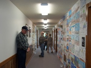 A hallway with walls covered in children's artwork, and a few people admiring it.
