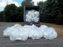 A truck overloaded with plastic bottles, many spilled onto the ground.