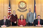 Five people posed in front of a wooden council backdrop with an American flag on one side.