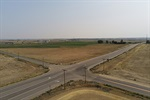 A rural intersection in an open field, with roads extending in four directions and sparse vegetation.
