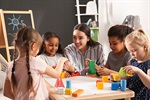 Children and a teacher playing with colorful blocks at a table in a classroom.