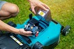 A person installing or removing a battery from a green robotic lawn mower on grass.