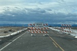 Road blocked with barriers, and a "ROAD CLOSED" sign under a cloudy sky.
