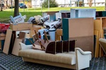 A pile of discarded furniture and household items, including a couch and various wooden pieces, on a paved outdoor area.