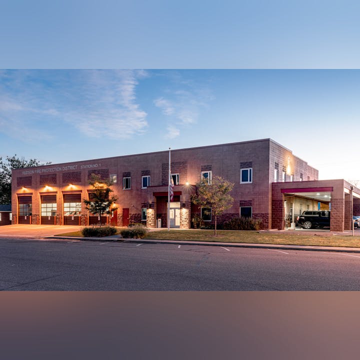 A fire station building with garages, an American flag, and trees at dusk.