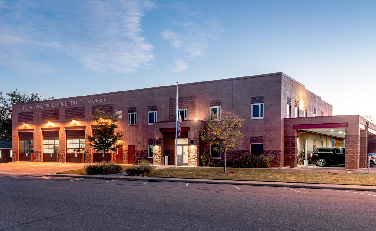 A fire station building with garages, an American flag, and trees at dusk.