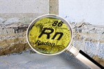 A magnifying glass showing "Radon," symbol "Rn," atomic number 86, over a cracked wall surface.