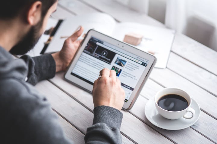 Male with beard, sitting at a table with a cup of coffee, researching data on a table