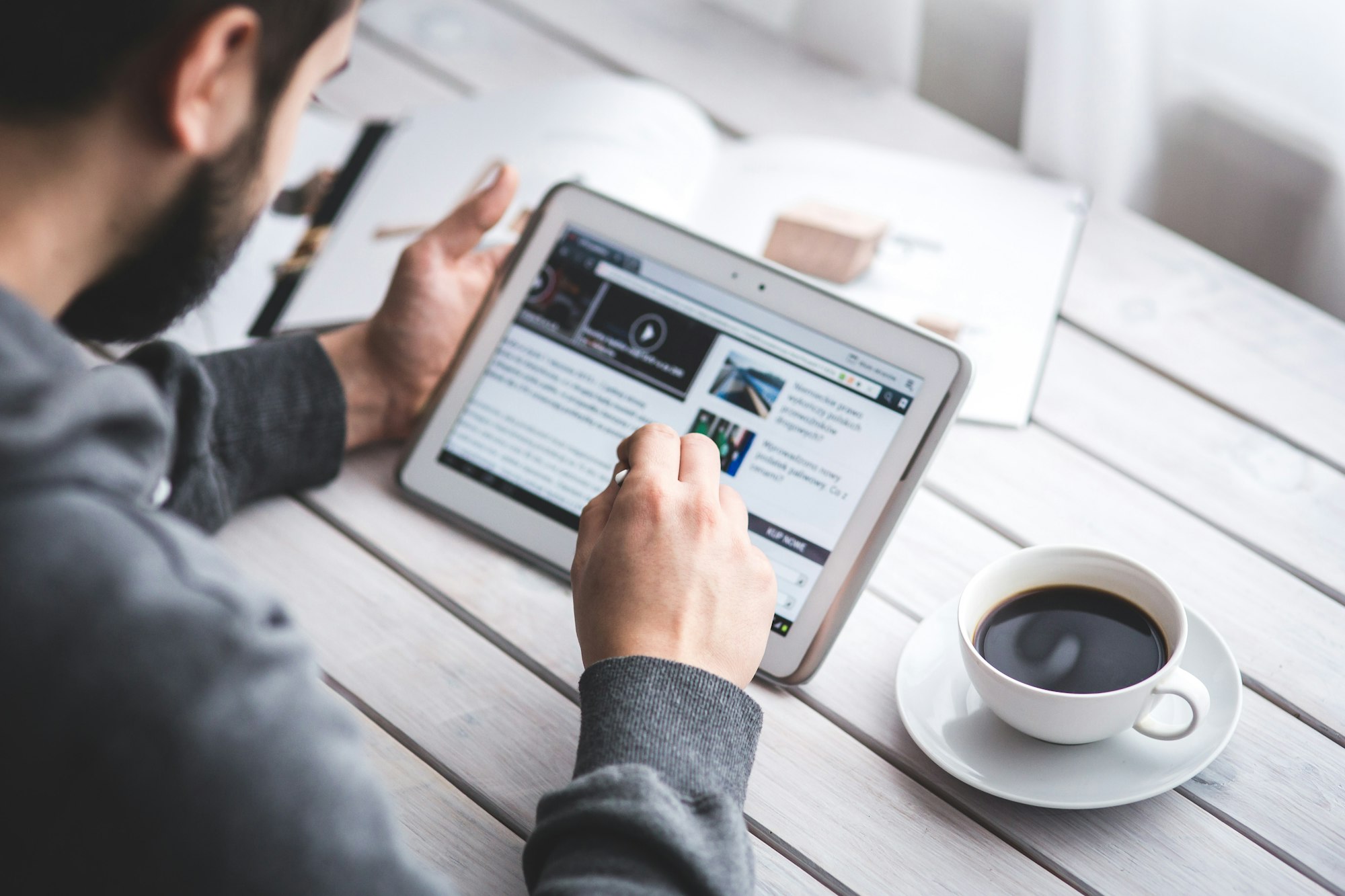 Male with beard, sitting at a table with a cup of coffee, researching data on a table