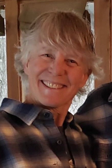 Board Member Mickey Naock - A smiling person with blond hair wearing a plaid shirt.