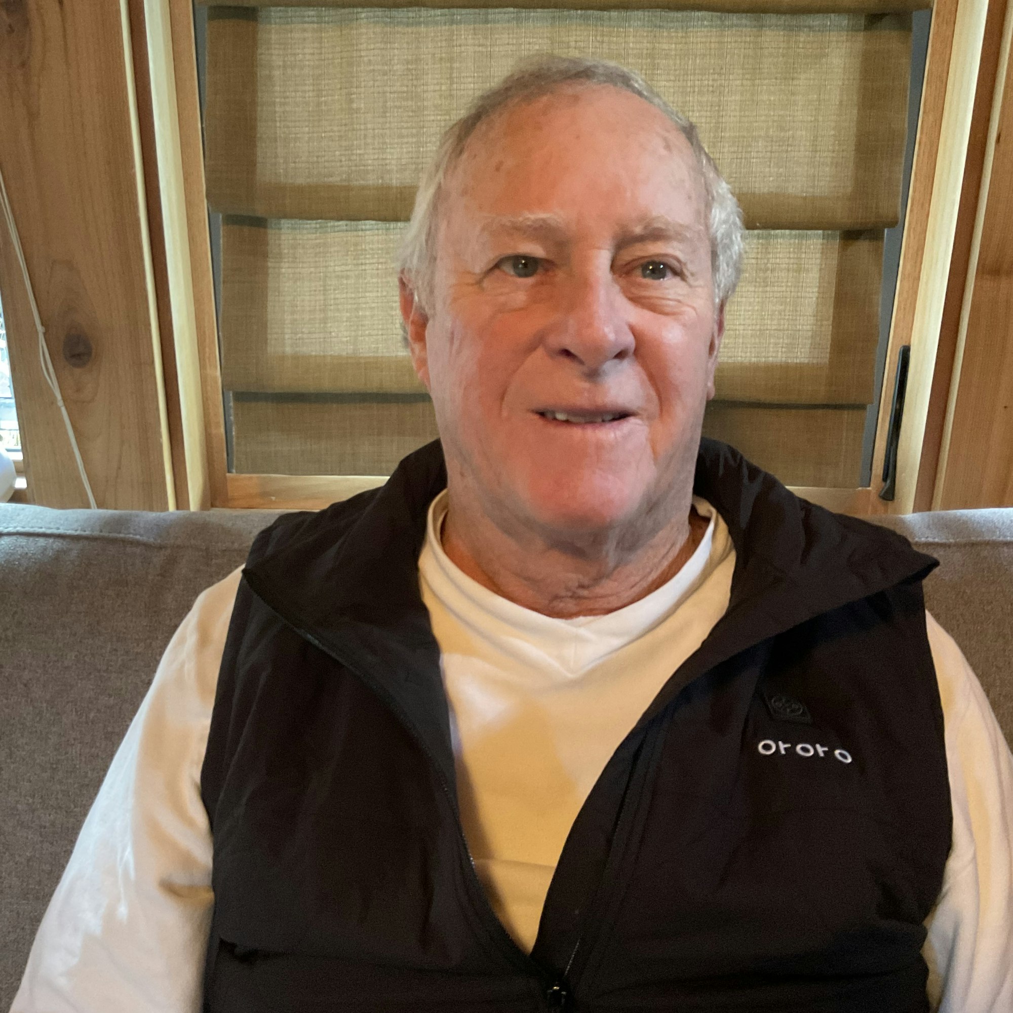 Smiling man wearing a vest and turtleneck indoors.