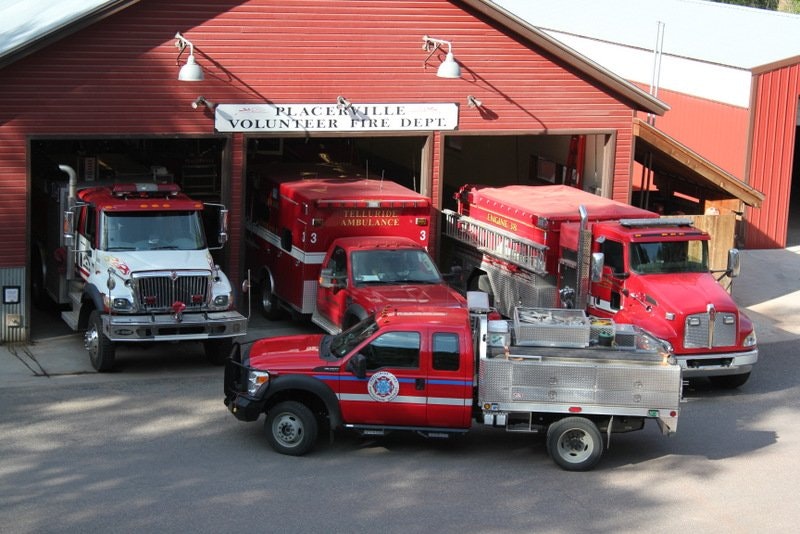 A red fire station garage with multiple fire trucks and an ambulance parked outside.