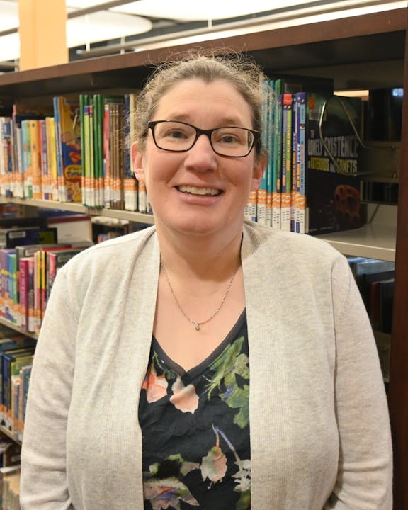 A person smiling in front of a library bookshelf filled with books.