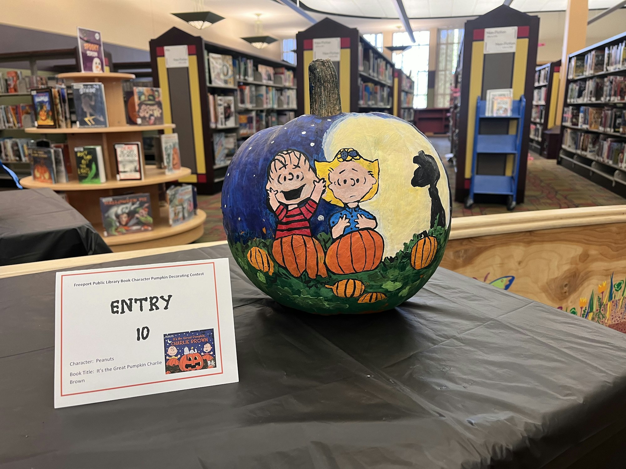 Painted pumpkin with Peanuts characters on display in a library contest, labeled "Entry 10."