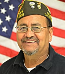 The image features a smiling man wearing a military cap, with an American flag in the background.