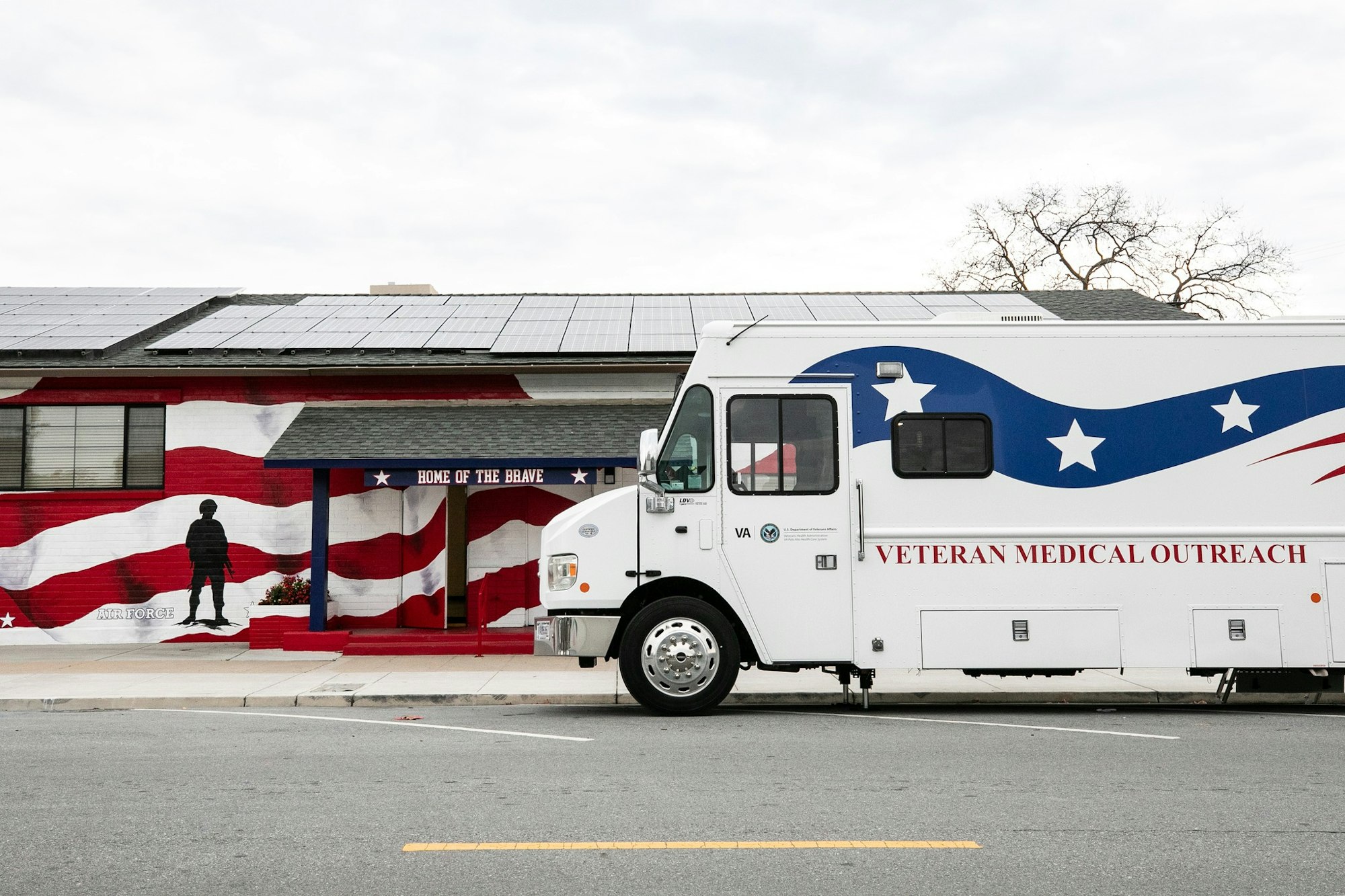 A medical outreach vehicle parked outside a building with a patriotic mural, promoting support for veterans.