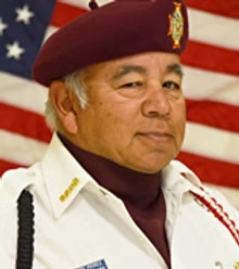 An individual in uniform with a maroon beret, posing in front of an American flag.