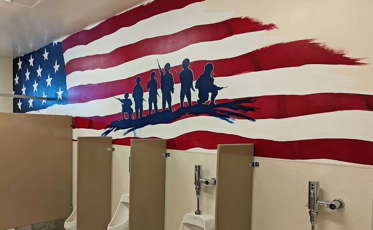 A mural of silhouetted figures against an American flag backdrop in a restroom setting, depicting themes of patriotism.