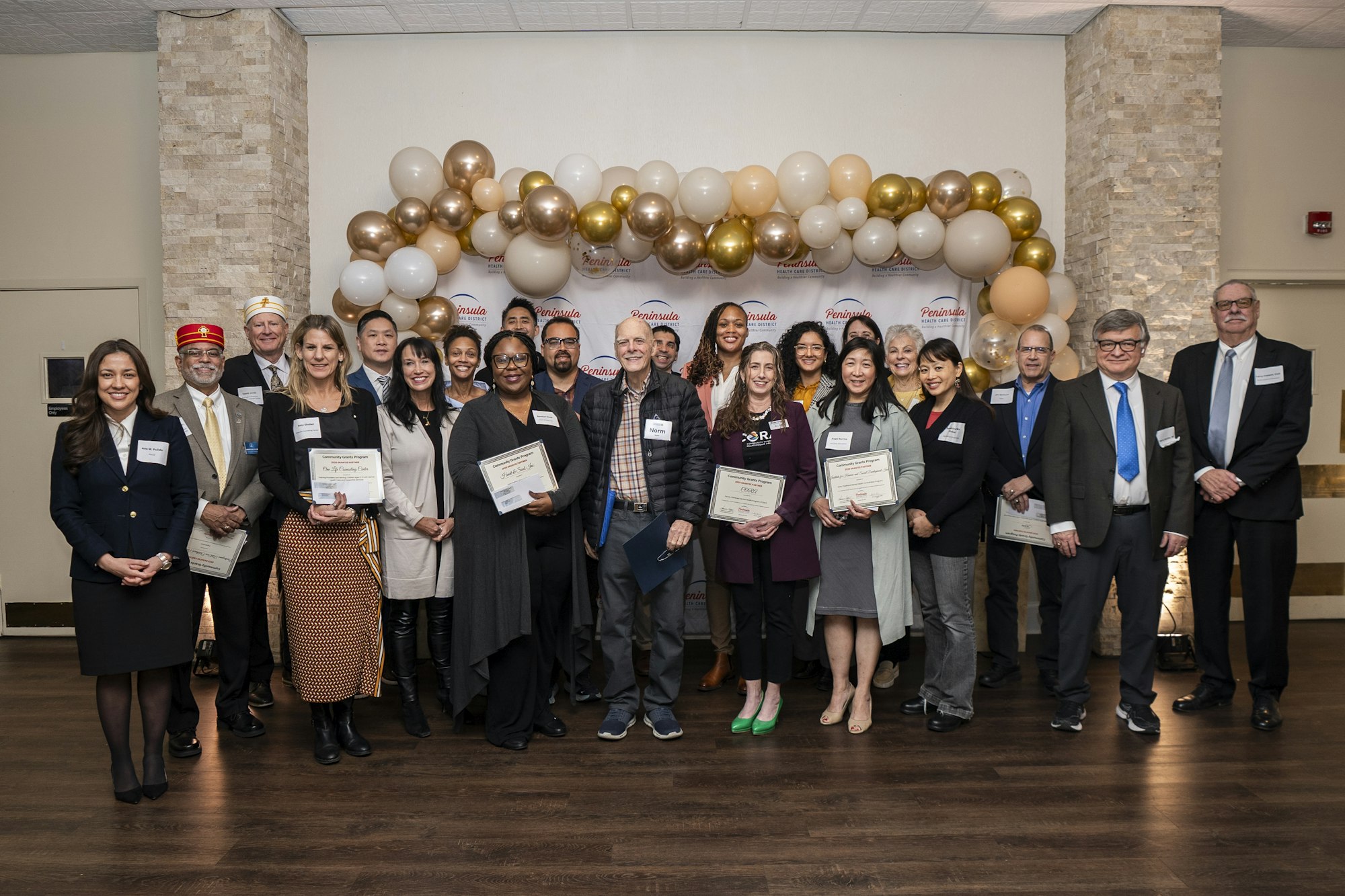 A group of people posing with certificates, standing in front of a backdrop with balloons.