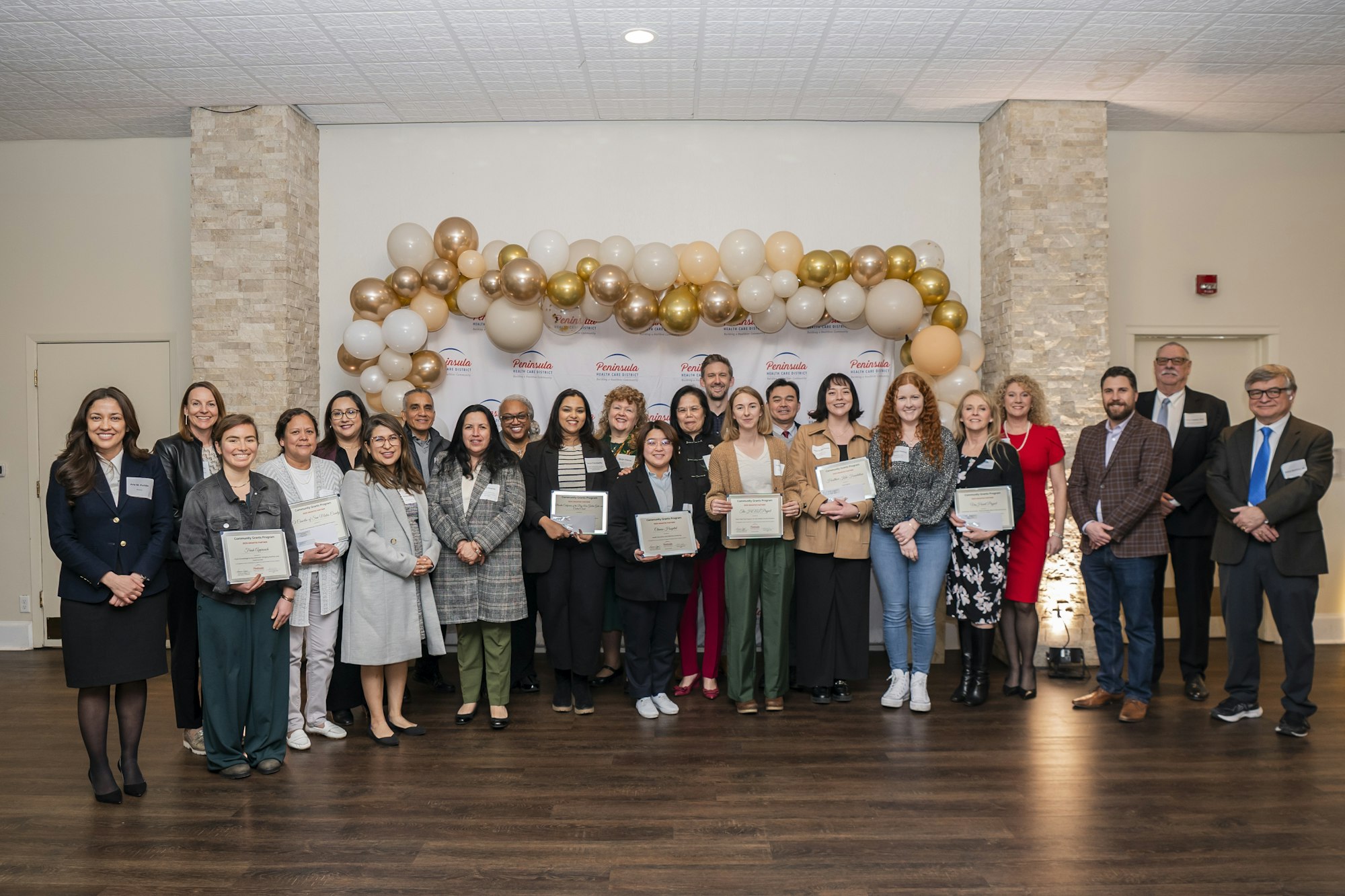 A group of people posing with certificates in front of a balloon and banner backdrop.