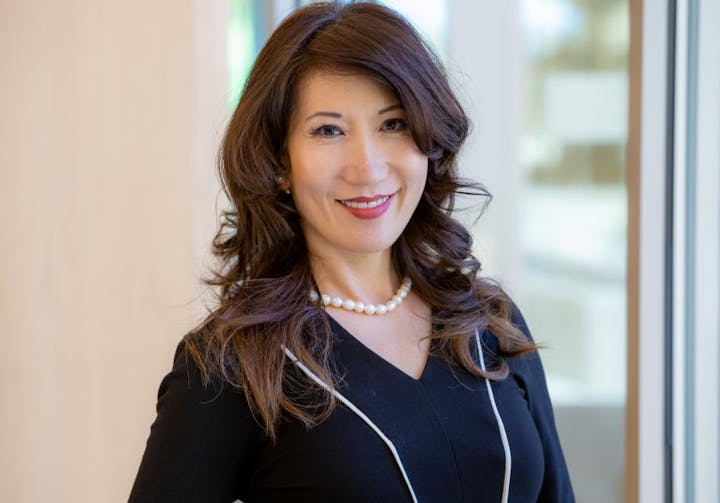 A professional woman smiling, wearing a black outfit and pearls.