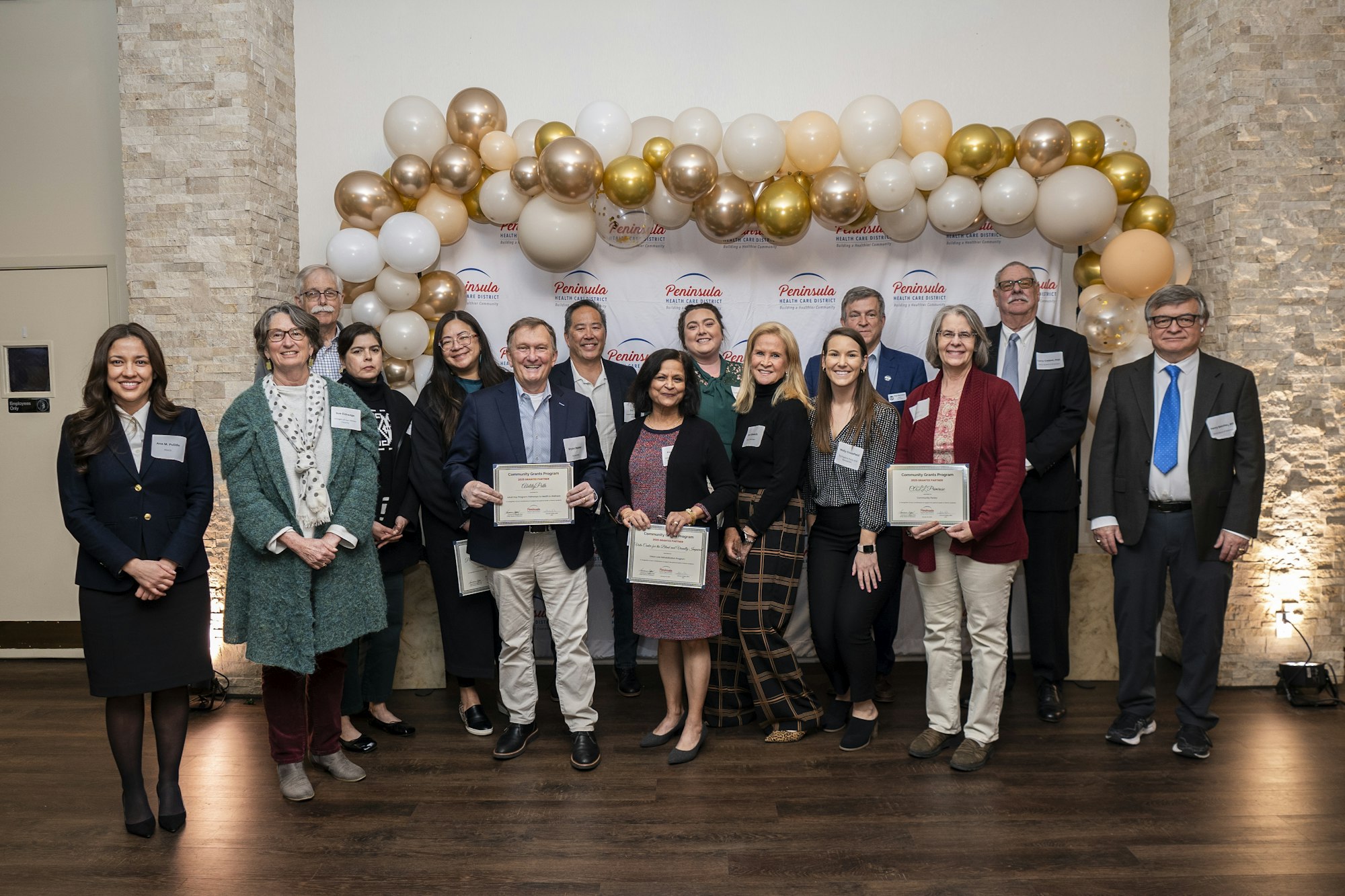 A group of people posing with certificates in front of a balloon arch and "Peninsula Health Care District" backdrop.