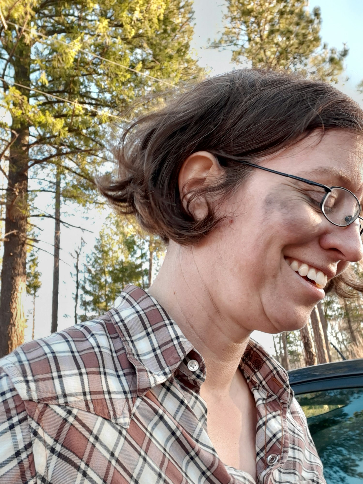 A smiling Euro-American woman wearing a flannel shirt and charcoal smudges on her face