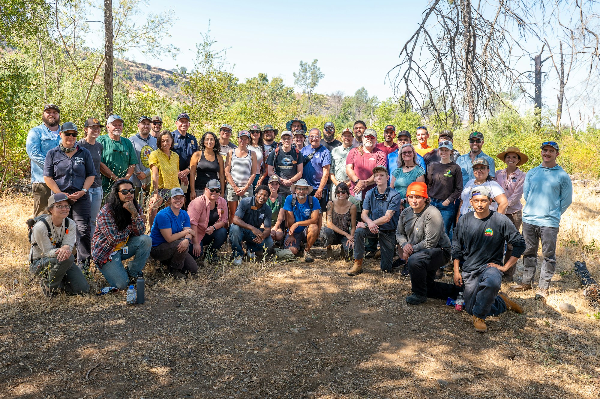 A large group of people posing together outdoors in a wooded area.