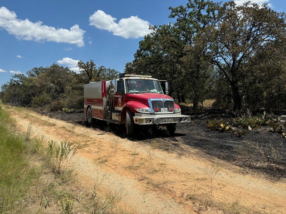 A fire truck parked on a dirt road next to a burnt area with trees and shrubbery.
